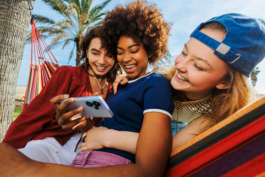 Friends laughing watching mobile phone on hammock