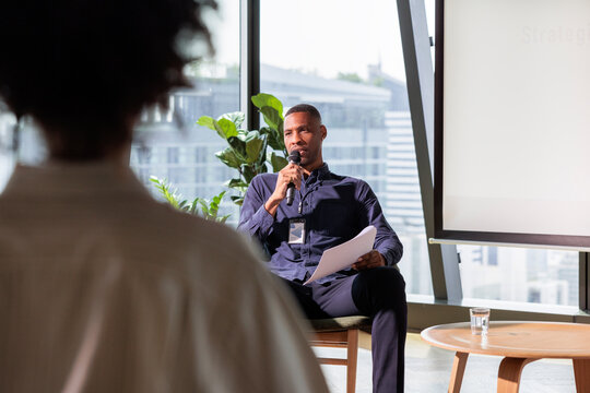 Speaker at a conference, holding a microphone and papers.