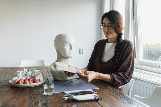 Female sculptor working on a white clay head bust in a bright studio.
