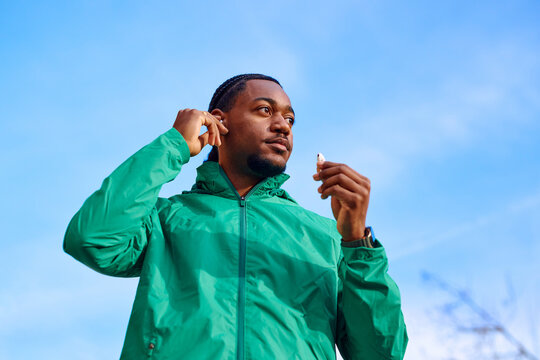 Black Young Adult Man Putting on Wireless Earbuds Outdoors