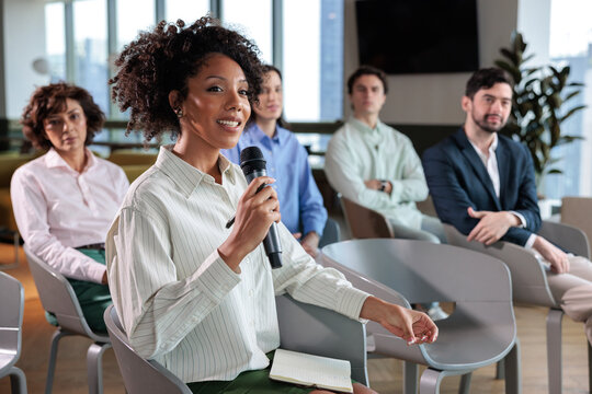 Woman speaks at meeting with diverse audience.