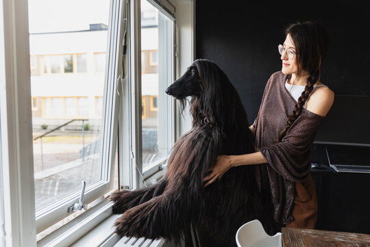 Woman and her Afghan Hound dog looking out through a large window