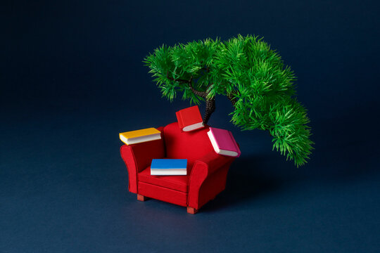 a red armchair with small colorful books beside a tree