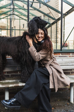 Smiling woman petting her Afghan Hound dog on an urban bench