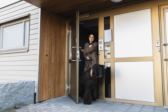 Woman opening a modern wooden door to step outside with her dog