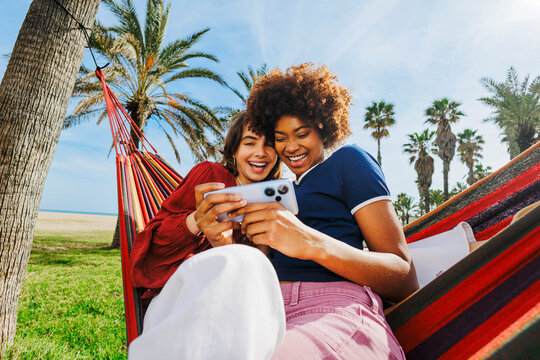 Friends laughing watching content on smartphone in hammock