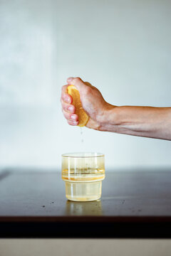 Hand Squeezing Lemon Over Glass With Water