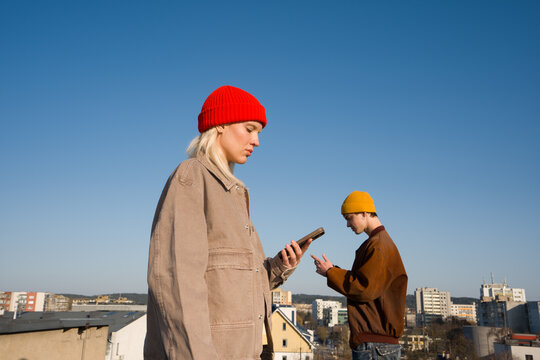 Two People Using Phones on a Rooftop Under Blue Sky