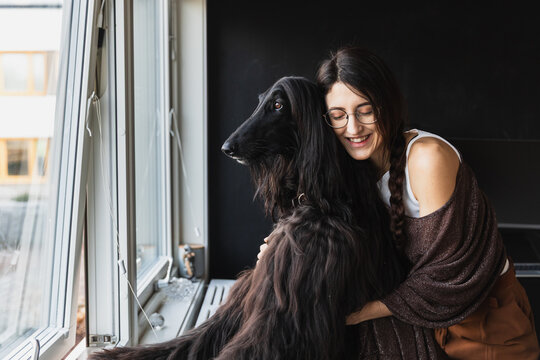 Woman embracing her black Afghan Hound dog by the window