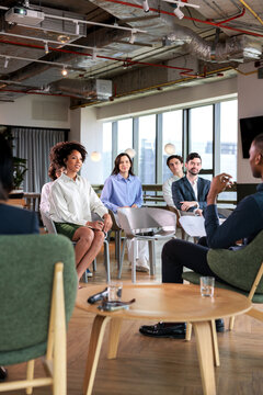 Diverse group listens to speaker in modern office space.