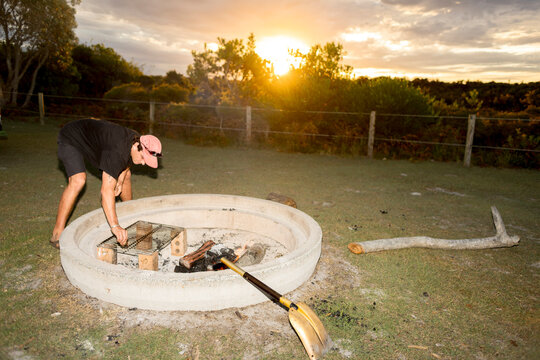 UGC Man adjusting fire pit grill at campsite in Australia at sunset