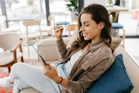 Young Woman Smiles While Holding a Tablet in a Bright Cafe