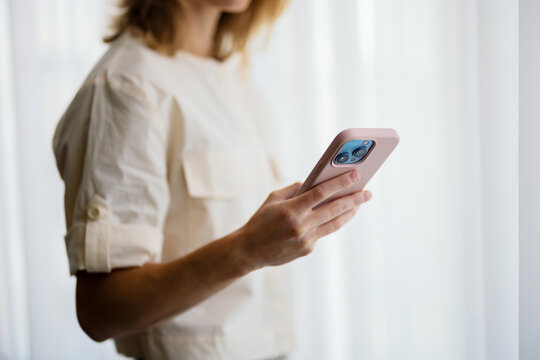Woman Holding Smartphone Near Window in Soft Light
