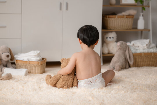 Young child in diaper sitting on fluffy carpet hugging teddy bear