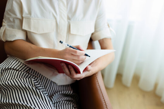 Woman Writing In Notebook While Sitting Indoors