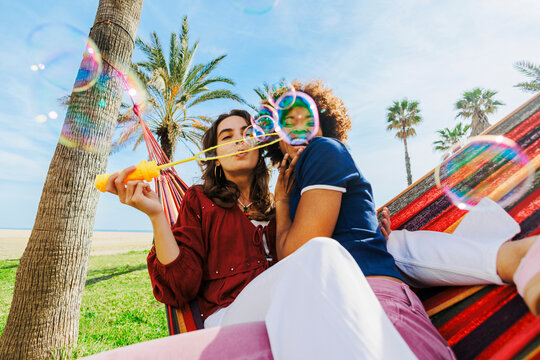 Friends blowing soap bubbles relaxing in beach hammock