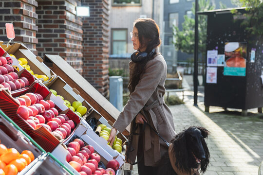 Woman choosing fresh apples at an outdoor market with her dog