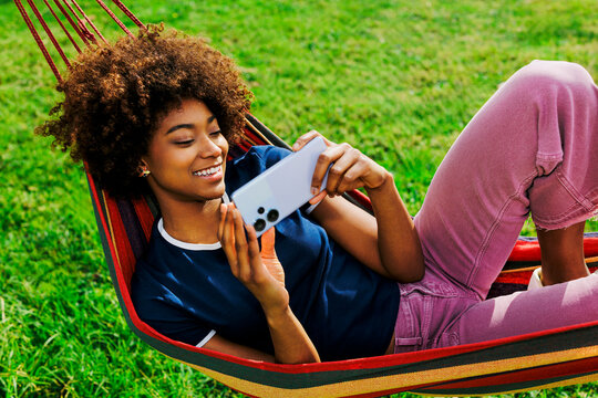 Smiling person relaxing on hammock using smartphone outdoors