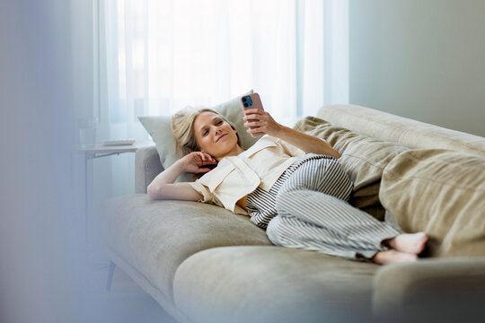 Relaxed Woman Lying On Couch Using Smartphone At Home