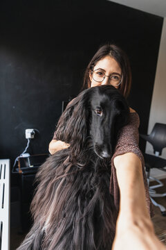 Young woman taking a selfie with her black Afghan Hound dog at home