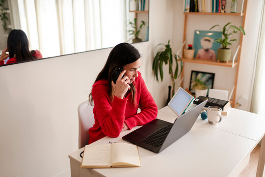 Focused Woman on Phone Call Reviewing Laptop at Home