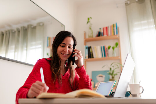 Delighted Woman Writing Notes During Phone Conversation