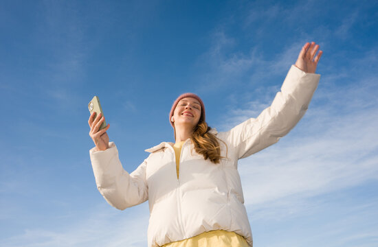 Woman Enjoys Time With Phone And Earbuds Under Blue Sky
