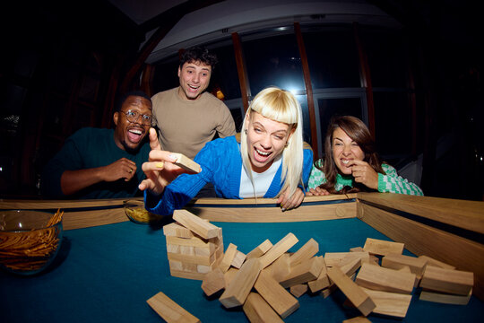 Group of Friends Playing a Game of Jenga at Night 