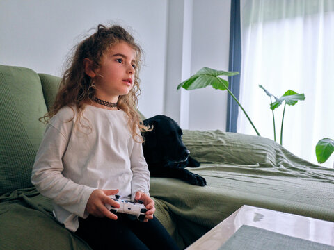 Young child playing video game with black dog