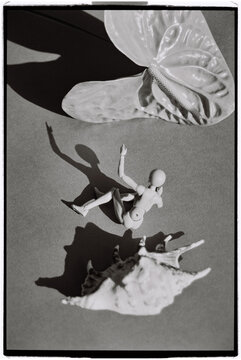 Figure resting near a shell and butterfly on a gray surface