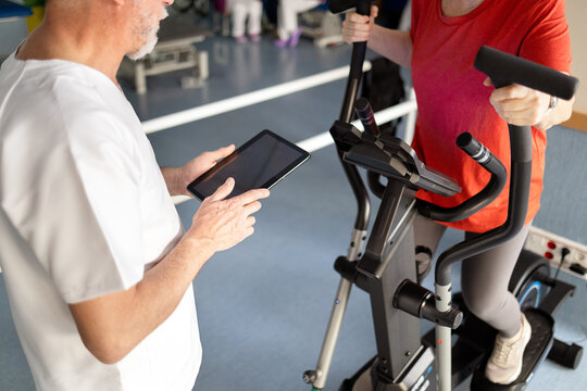 Physiotherapist guiding woman on elliptical with tablet