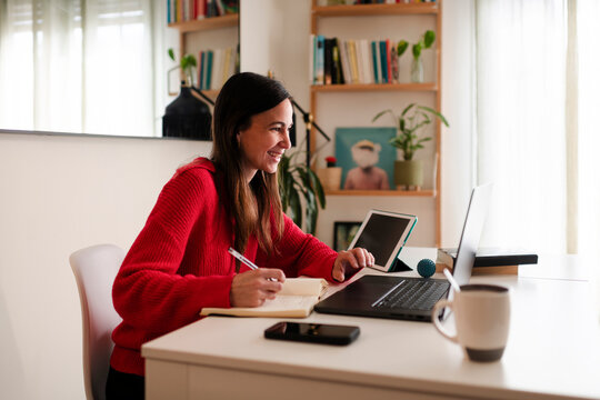 Cheerful Woman Taking Notes During Video Call at Home Office
