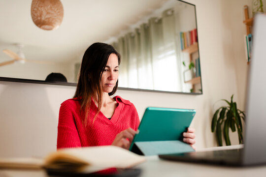 Focused Woman Reading on Tablet at Home Desk