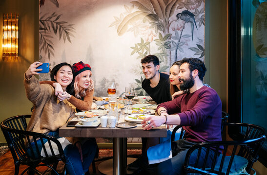 Diverse friends enjoying dinner taking selfie at restaurant