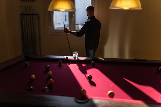 Man with billiard cue standing by window in backlight