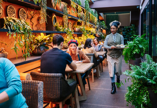 Black waitress serving guests at green indoor restaurant