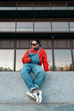 Young man using smartphone sitting on urban wall