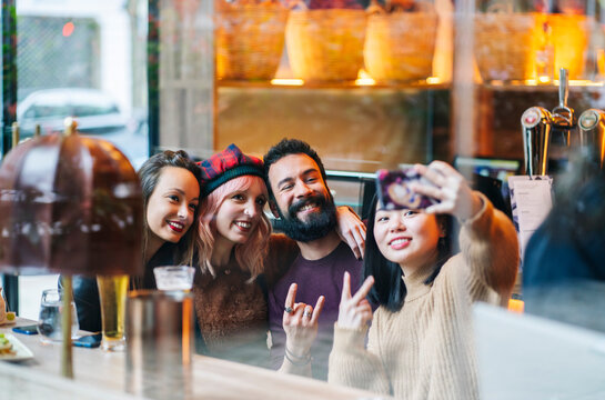 Diverse friends capturing group selfie at bar restaurant