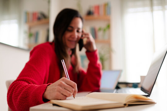 Smiling Woman Writing Notes While Talking on Phone