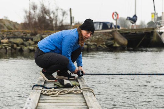 Woman Sailor Mooring Sailboat to Wooden Dock in Marina