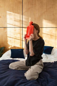 Person holding hot water bottle to face for pain relief