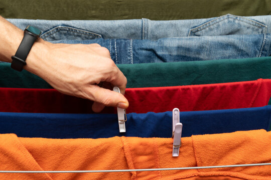 Hand clipping colorful clothes on drying rack with clothespins