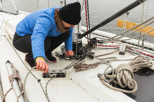 Female Sailor Crouching by Mast to Adjust Rigging and Lines