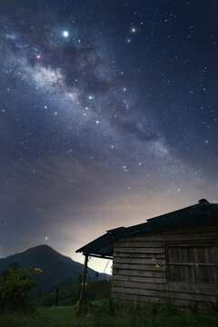 Milky way arching over old wooden cabin at night