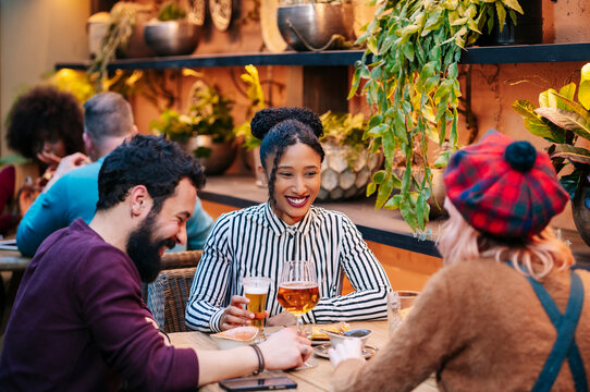 Diverse friends enjoying drinks and laughing at restaurant patio