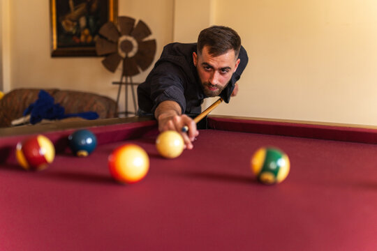 Elegant man playing billiards aiming shot at home