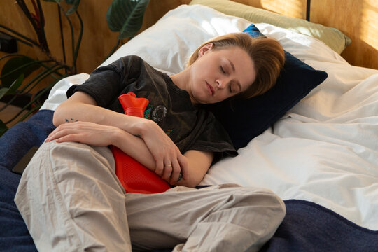 Person experiencing menstrual cramps using heating pad in bed