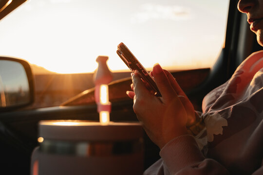 Person holding smartphone in car during sunset golden hour