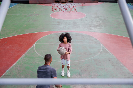 Father and daughter playing basketball on an outdoor court.