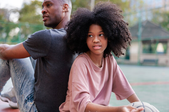 Father and daughter sit back-to-back with a basketball.